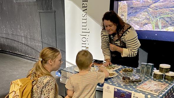 Bild med mamma och barn som får provsmaka sjömat på Universeum.